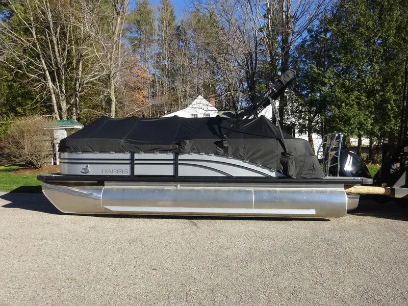 Slide: The Image of 2024 Harris Sunliner 210 pontoon boat with black cover, parked outdoors. - 2