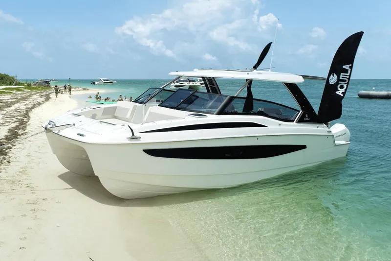 Slide: The Image of 2023 Aquila 32 Sport boat anchored on a sandy beach with people in the background. - 0
