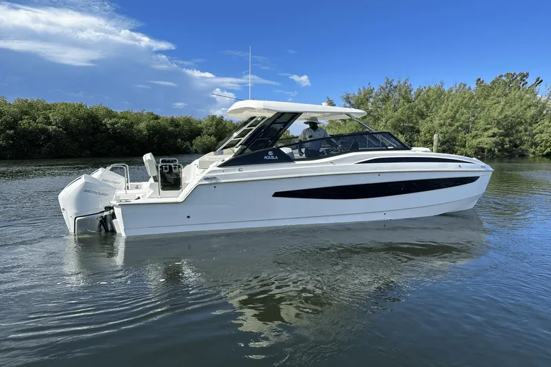 Slide: The Image of 2023 Aquila 32 Sport boat cruising on a calm river with lush greenery. - 1