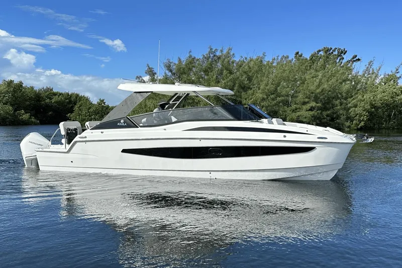 Slide: The Image of 2023 Aquila 32 Sport boat on calm water with lush greenery in the background. - 2