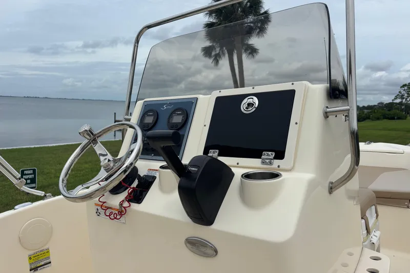 Slide: The Image of 2024 Scout 175 Sportfish boat console with steering wheel and controls, near a serene waterfront. - 9