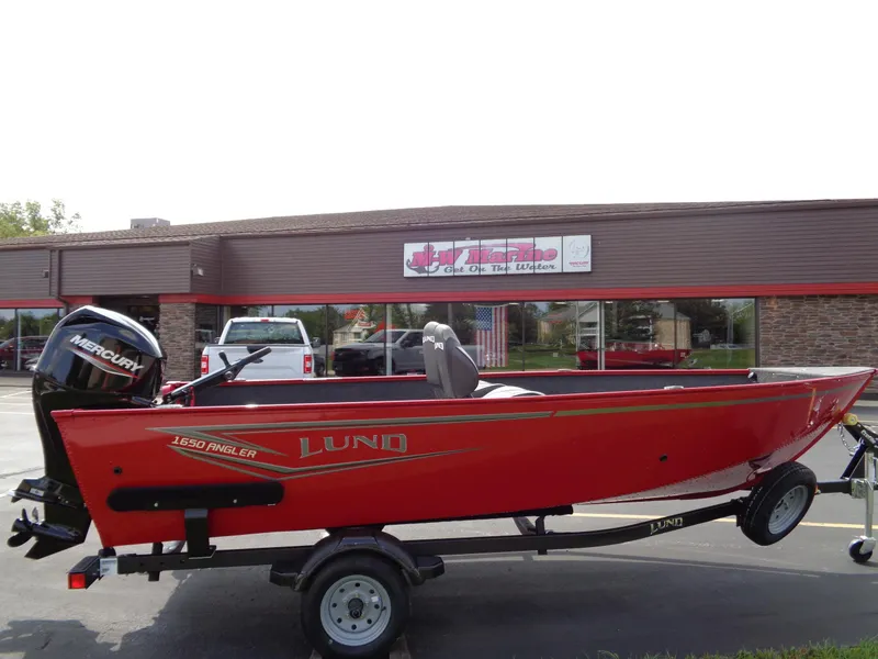 Slide: The Image of 2024 Lund 1650 Angler boat in red, parked on a trailer outside a dealership. - 1