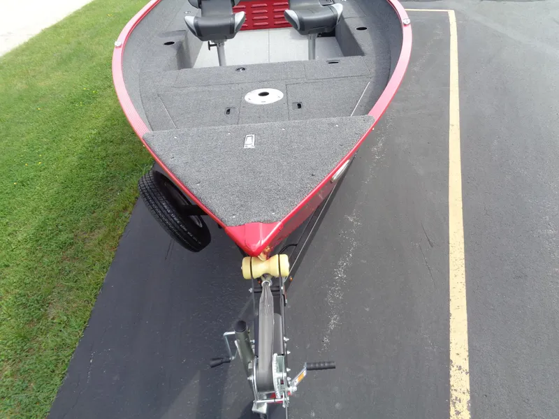 Slide: The Image of 2024 Lund 1650 Angler boat on trailer, red exterior, spacious deck, parked on asphalt. - 5
