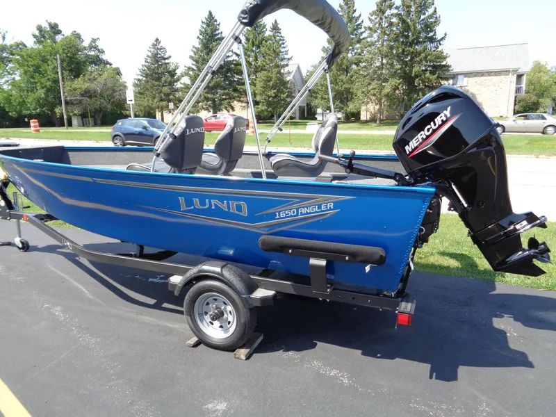 Slide: The Image of 2024 Lund 1650 Angler boat with Mercury engine on trailer, parked outdoors. - 1