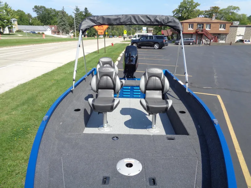 Slide: The Image of 2024 Lund 1650 Angler boat with seating and canopy, parked on pavement. - 4
