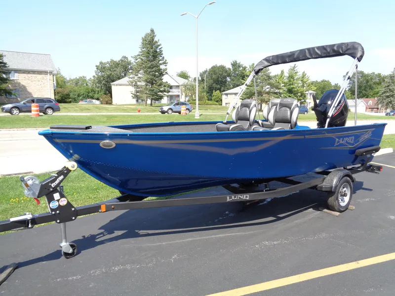 Slide: The Image of 2024 Lund 1650 Angler boat on trailer, blue exterior, parked outdoors. - 5