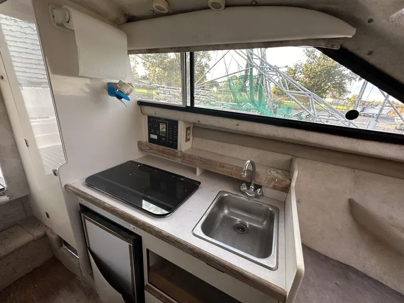 Slide: The Image of 1998 Bayliner 2452 Ciera Express boat interior kitchen with sink, stove, and window view. - 15