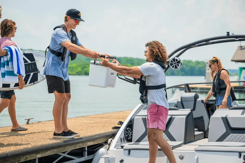 Slide: The Image of People enjoying a day on a 2024 Yamaha Boats 222XD, transferring a cooler. - 46