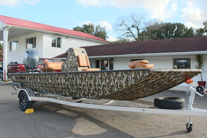 Slide: The Image of 2024 Avid 20 Rogue boat on trailer, camo design, parked outside building. - 11