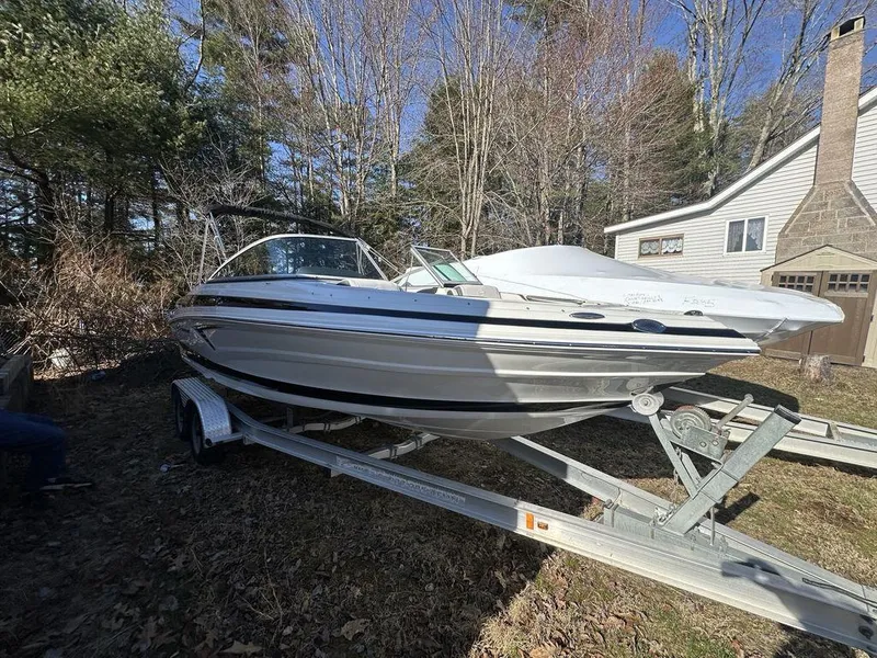 Slide: The Image of 2024 Crownline SS Series 220 boat on a trailer in a wooded yard. - 2