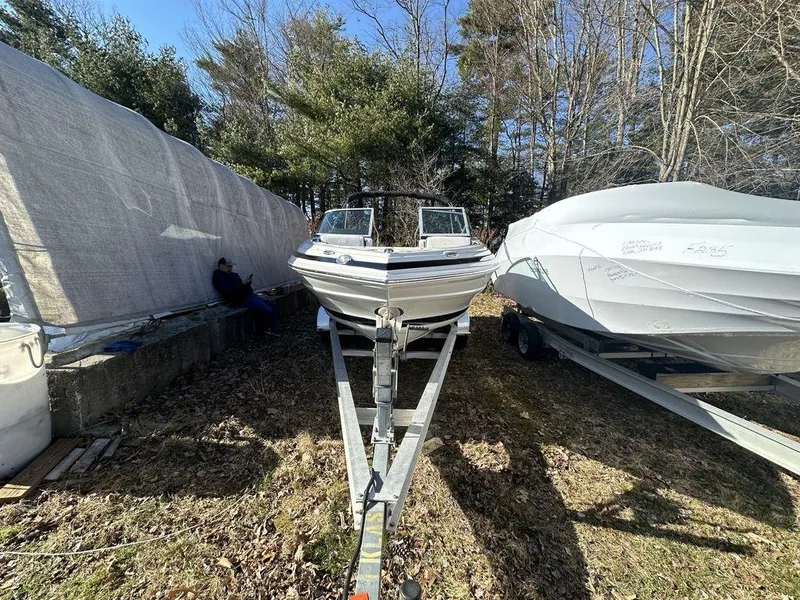 Slide: The Image of 2024 Crownline SS Series 220 boat on a trailer, parked outdoors between two covered boats. - 9