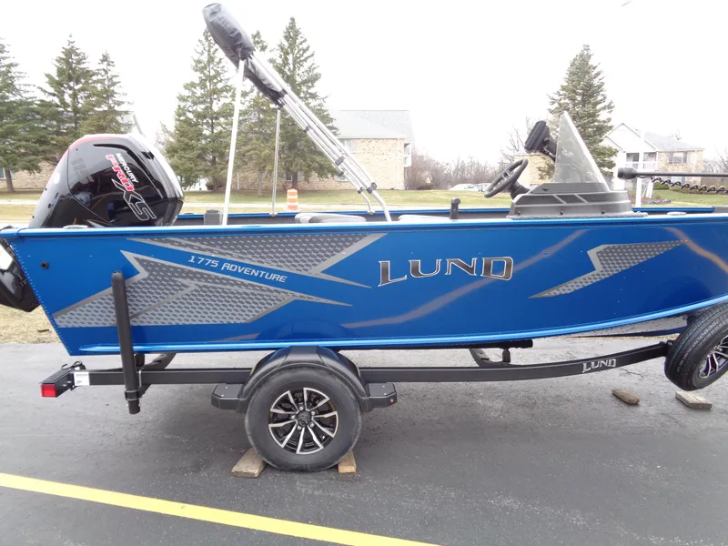 Slide: The Image of 2024 Lund 1775 Adventure SS boat, blue exterior, on trailer, parked outdoors. - 3