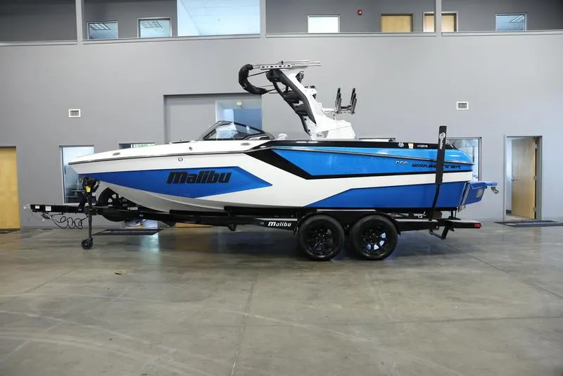 Slide: The Image of 2024 Malibu 23 MXZ boat in showroom, blue and white exterior, on trailer. - 0