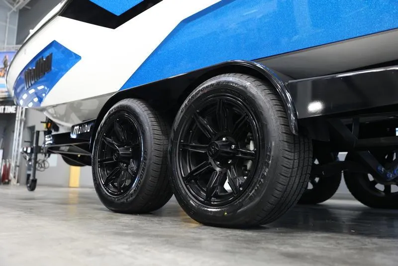 Slide: The Image of 2024 Malibu 23 MXZ boat trailer with black wheels in a showroom. - 12