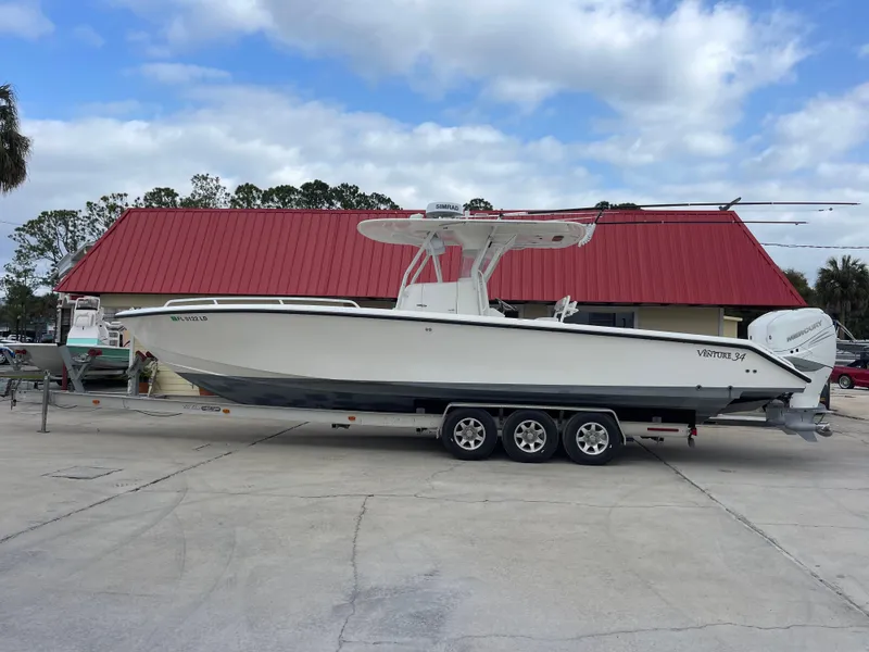 The Image of 1999 Venture 34 Center Console boat on a trailer in front of a red-roofed building. - 1