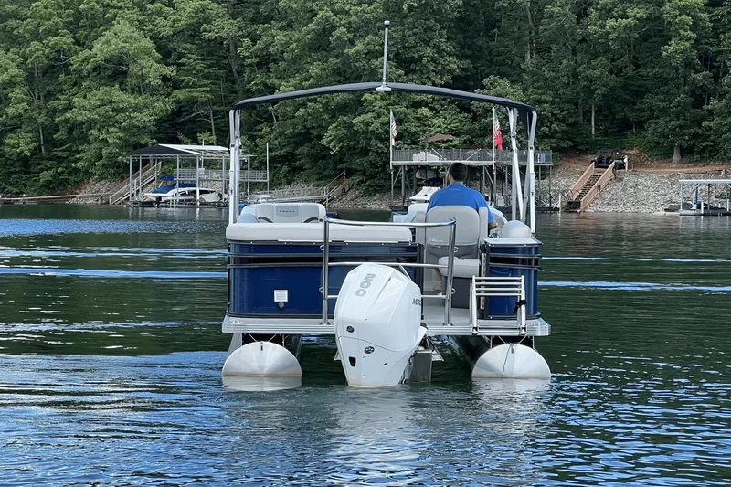 Slide: The Image of 2023 Crest Classic DLX 220 pontoon boat on a serene lake with lush green surroundings. - 2