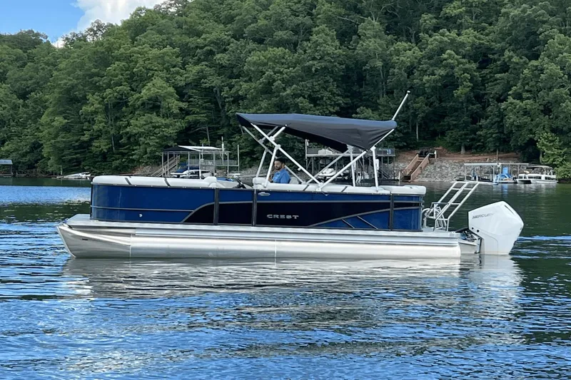 Slide: The Image of 2023 Crest Classic DLX 220 pontoon boat on a serene lake with lush green trees. - 4