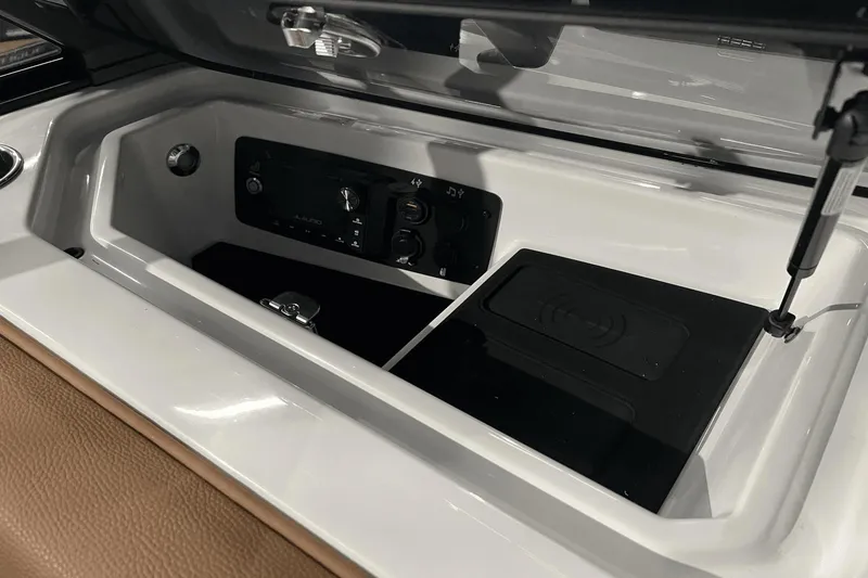Slide: The Image of 2023 Nautique Super Air Nautique S25 storage compartment with audio controls and wireless charging pad. - 21