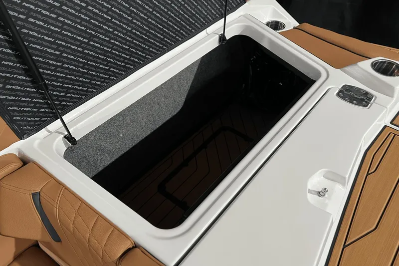 Slide: The Image of 2023 Nautique Super Air Nautique S25 storage compartment with tan upholstery and cup holders. - 7