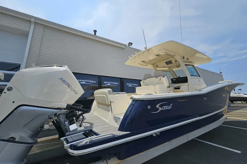 Slide: The Image of 2024 Scout 305 LXF boat with Mercury engine, parked outside a dealership. - 2