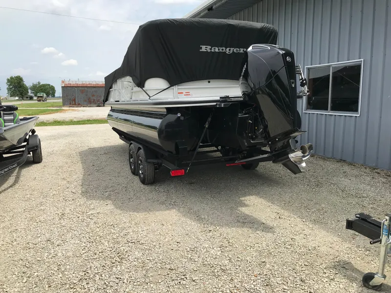 Slide: The Image of 2024 Ranger Reata 223C boat with cover, parked on gravel near a building. - 20