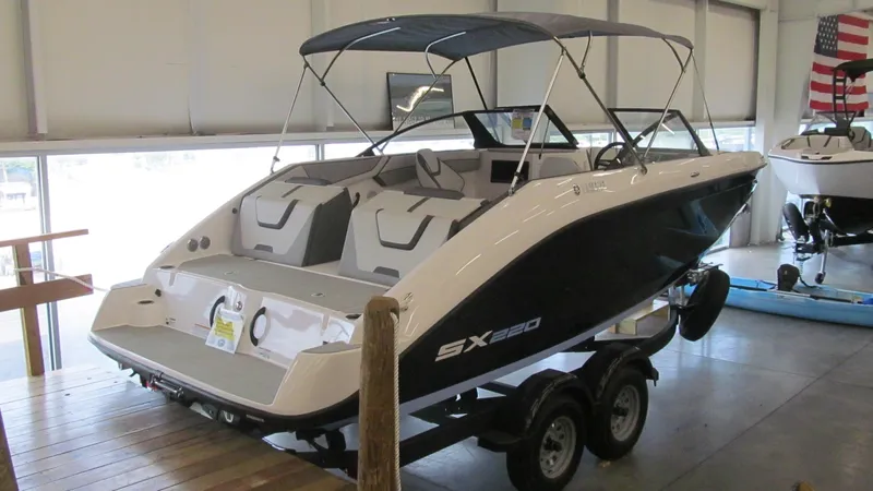 Slide: The Image of 2024 Yamaha Boats SX220 in showroom, sleek design, dual axle trailer, American flag in background. - 2