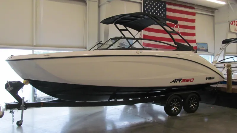 Slide: The Image of 2024 Yamaha AR250 boat on trailer in showroom with American flag backdrop. - 0