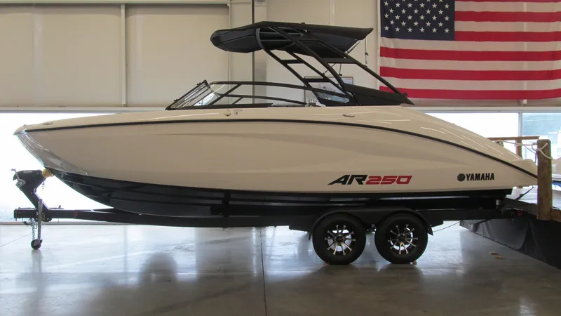Slide: The Image of 2024 Yamaha AR250 boat on trailer, indoors, with American flag backdrop. - 1