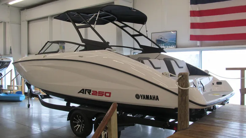 Slide: The Image of 2024 Yamaha AR250 boat displayed indoors with American flag backdrop. - 2