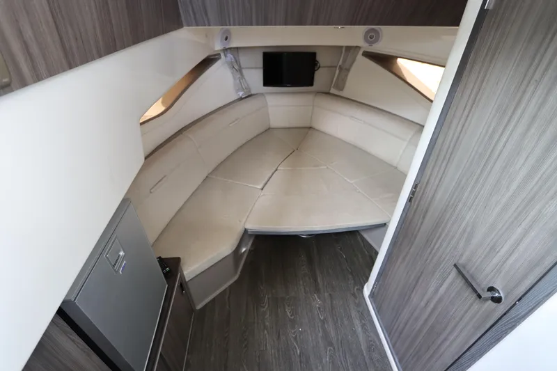Slide: The Image of 2019 Sea Ray Sundancer 320 cabin interior with seating, wood paneling, and a small TV. - 35