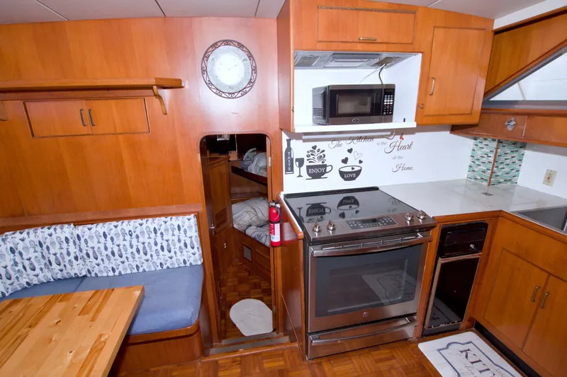 Slide: The Image of 1994 Jefferson Marquessa 56 yacht kitchen with wood cabinetry, stove, microwave, and cozy dining area. - 60