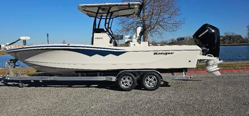 Slide: The Image of 2024 Ranger 2660 Bay boat on trailer by a lake. - 0