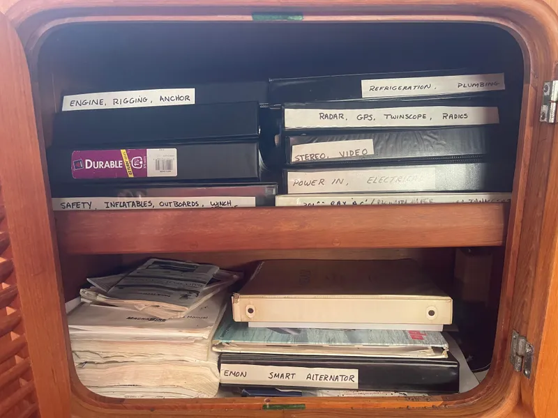 Slide: The Image of Organized manuals and binders in a wooden cabinet on a 1995 Passport 47 AC Plan B sailboat. - 32