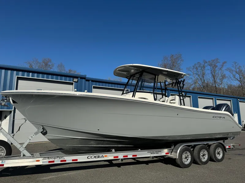 Slide: The Image of 2021 Cobia 301 CC boat on trailer, parked outside blue warehouse. - 1