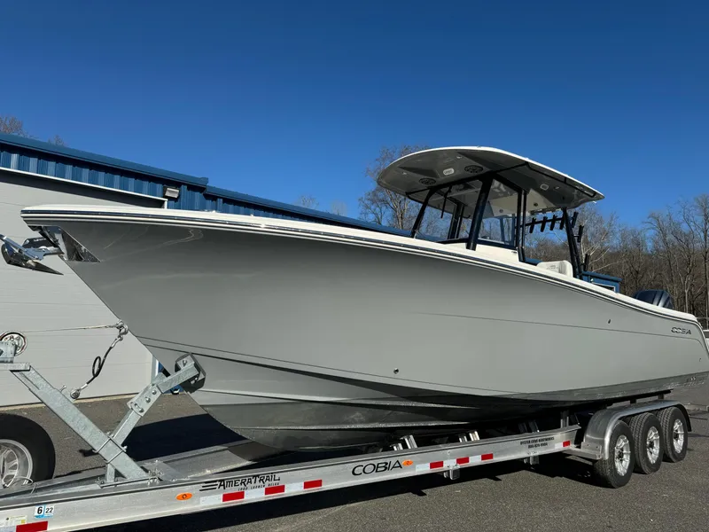 Slide: The Image of 2021 Cobia 301 CC boat on trailer, parked outdoors under clear blue sky. - 2