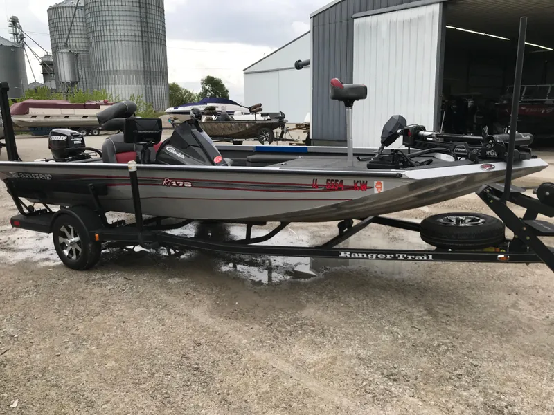 Slide: The Image of 2018 Ranger RT178 fishing boat on trailer, parked near a metal building. - 49