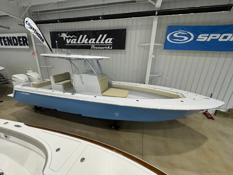 Slide: The Image of 2025 Contender 32 ST boat in showroom, blue hull, white interior, Valhalla and Sport banners. - 3