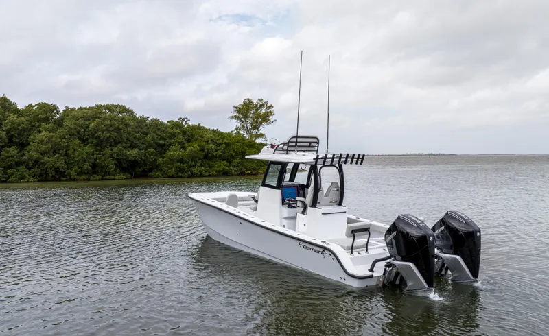 Slide: The Image of 2024 Freeman 28 boat with dual outboard motors on a calm lake. - 12