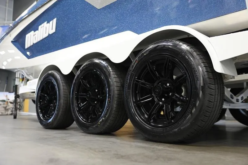 Slide: The Image of 2024 Malibu 24 MXZ boat trailer with black wheels in a showroom. - 11