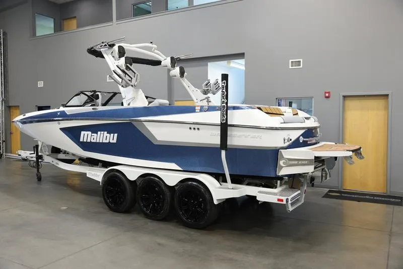 Slide: The Image of 2024 Malibu 24 MXZ boat in showroom, blue and white exterior, on a trailer. - 15