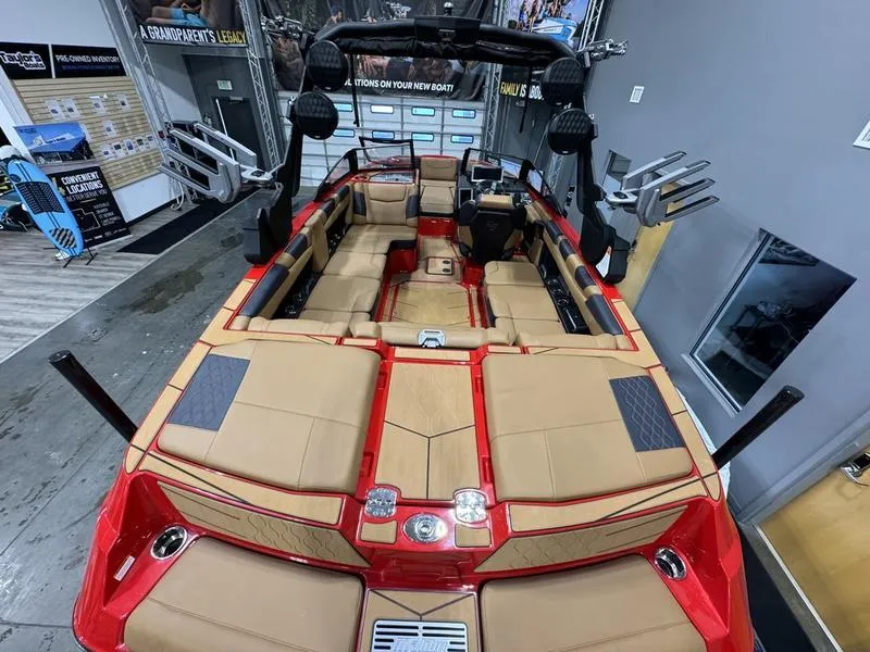 Slide: The Image of 2024 Malibu M220 boat interior with tan seats and red accents in showroom. - 2