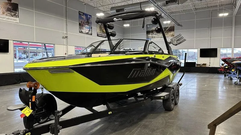 Slide: The Image of 2024 Malibu 22 LSV boat in showroom, black and yellow design, on trailer. - 2
