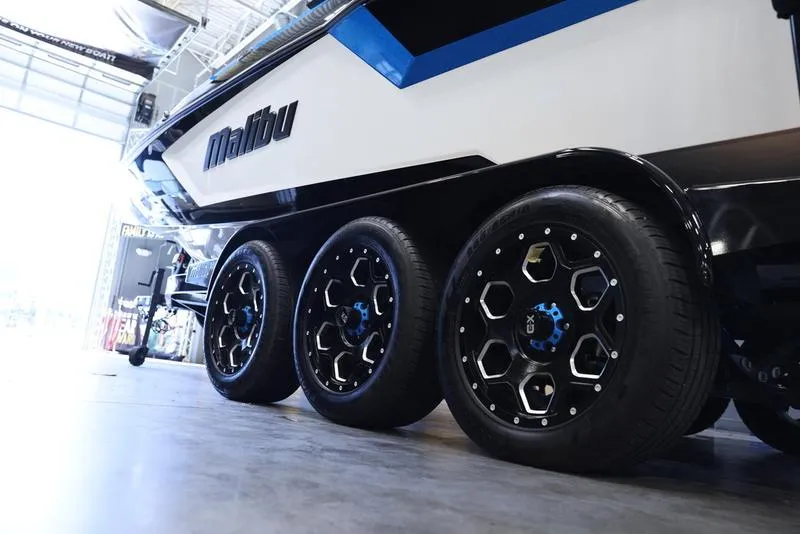 Slide: The Image of 2024 Malibu 24 MXZ boat on a triple-axle trailer in a showroom. - 7