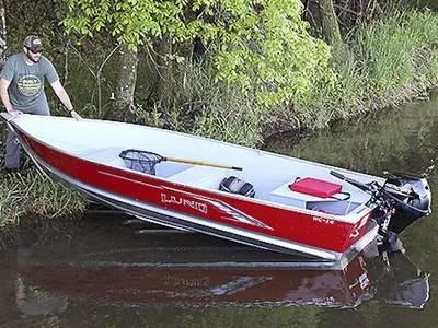 The Image of 2024 Lund WC-14 Tiller boat in water near a forested shoreline. - 1