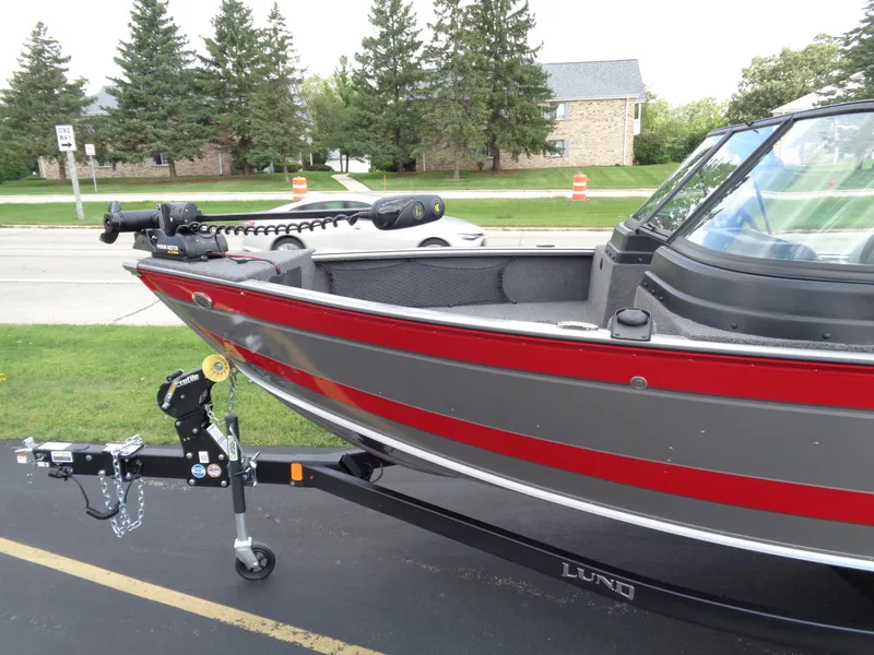 Slide: The Image of 2024 Lund 1875 Impact XS boat on trailer, parked near road with trees in background. - 16