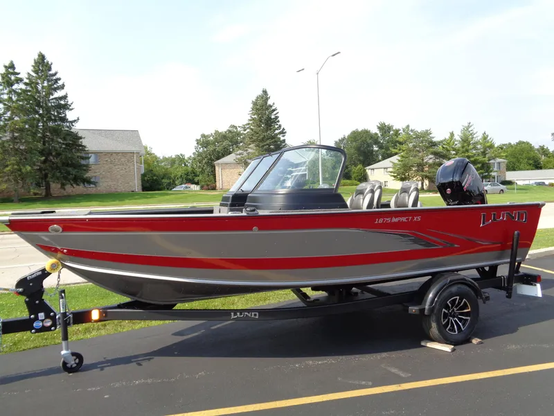 Slide: The Image of 2024 Lund 1875 Impact XS boat on trailer, red and gray design, parked outdoors. - 2