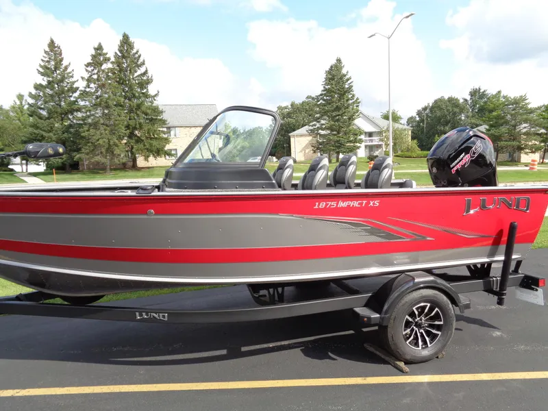 Slide: The Image of 2024 Lund 1875 Impact XS boat on trailer, red and gray design, parked outdoors. - 29