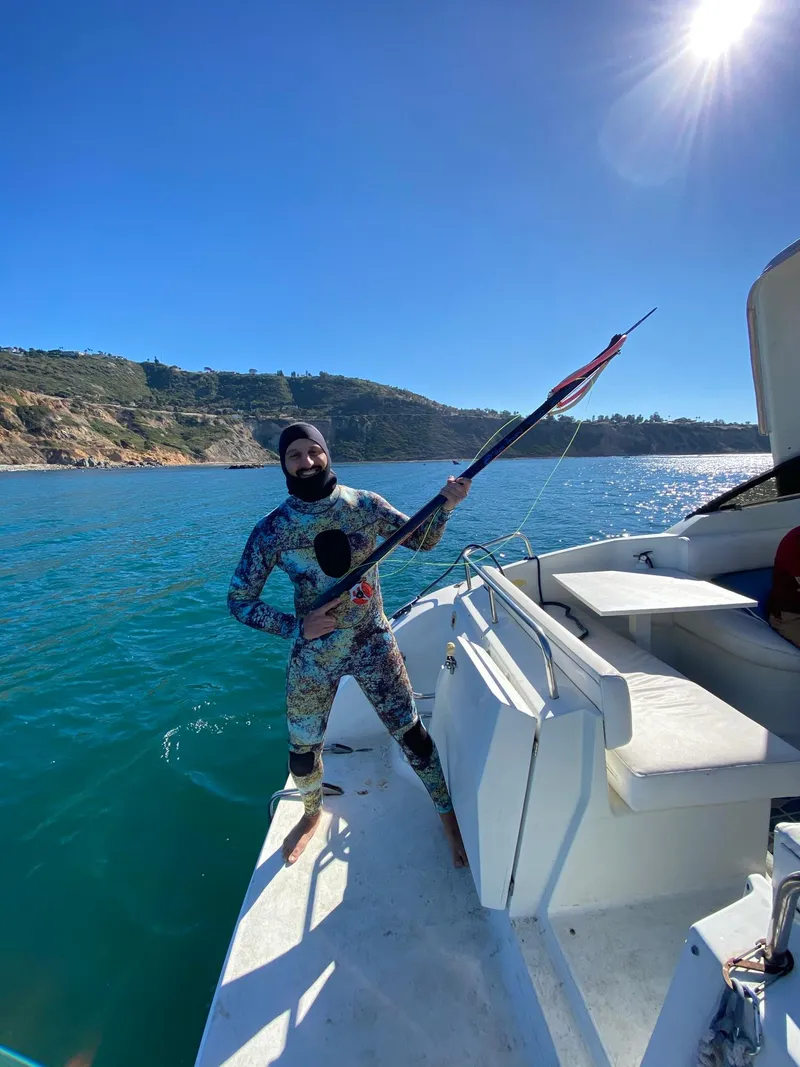Slide: The Image of Man in wetsuit holding spear on 1993 Silverton 38 Express boat in scenic coastal waters. - 12