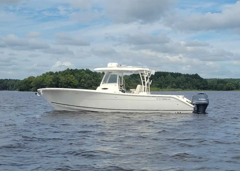 Slide: The Image of 2019 Cobia 320 CC boat on a calm lake under a cloudy sky. - 2