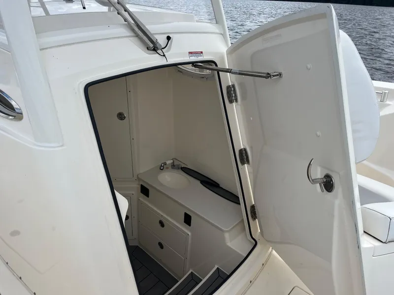 Slide: The Image of 2019 Cobia 320 CC boat interior with open door, showing compact sink and storage. - 36